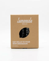 A lemonade dolls box with the brand name on it and three pairs of black lace thongs in it 