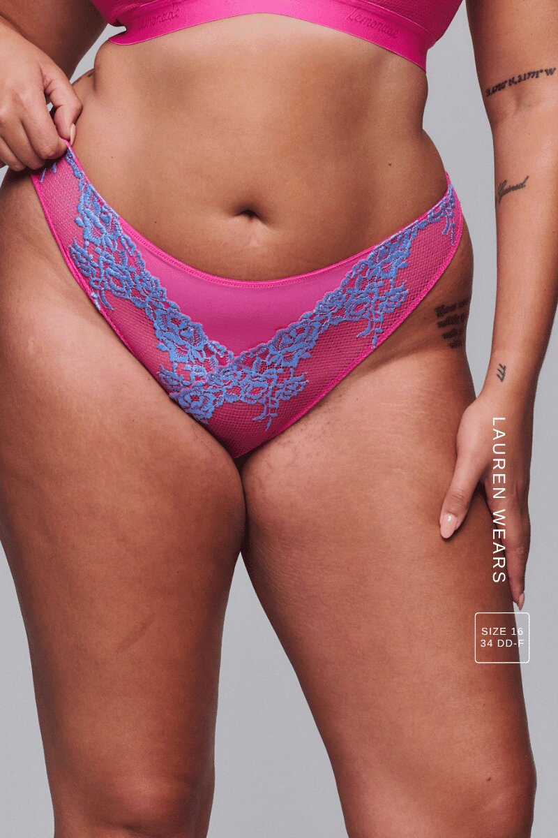 A woman modelling a pink lace embroidered bralette with a matching thong