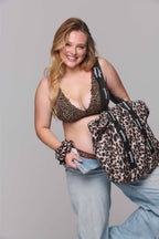 Woman wearing leopard print top and holding a matching bag against a gray background