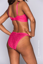 A woman standing with her back to, wearing a pink lace bralette called "iridescent" paired with matching knickers 