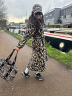 Person wearing a leopard print coat and hat, holding a matching bag, walking along a path by a canal.