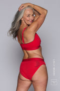 A woman standing with her back to, wearing a red mesh fuller cup bralette paired with a matching brief 
