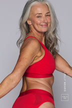 A woman looking back at the camera, wearing a red mesh fuller cup bralette paired with a matching brief