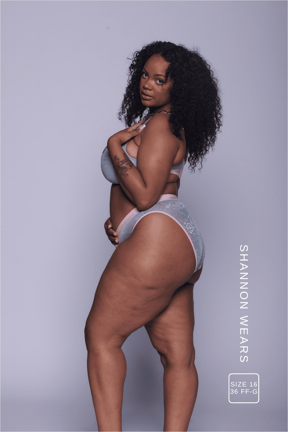 A woman standing with her side to wearing a light blue lace fuller cup bralette with a pink band with matching briefs 