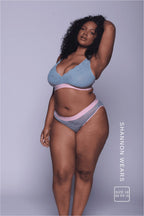 A woman standing with her hand in the hair wearing a light blue lace fuller cup bralette with a pink band with matching briefs 