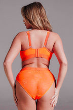 A woman standing with her back to, wearing the signature lace fuller cup bralette in neon orange paired with the matching brief