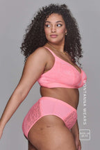 Woman wearing a high support coral bra called The One paired with matching knickers