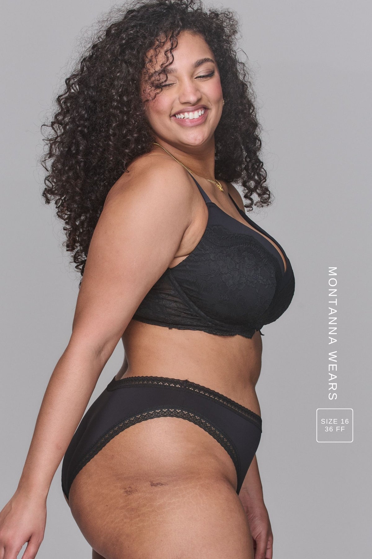 A woman smiling standing with her side to, modelling a Black V Brazilian paired with a matching black bra with lace details 