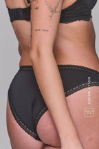 A close up image of a woman standing with her back to, wearing a Black V Brazilian called "The Flex"