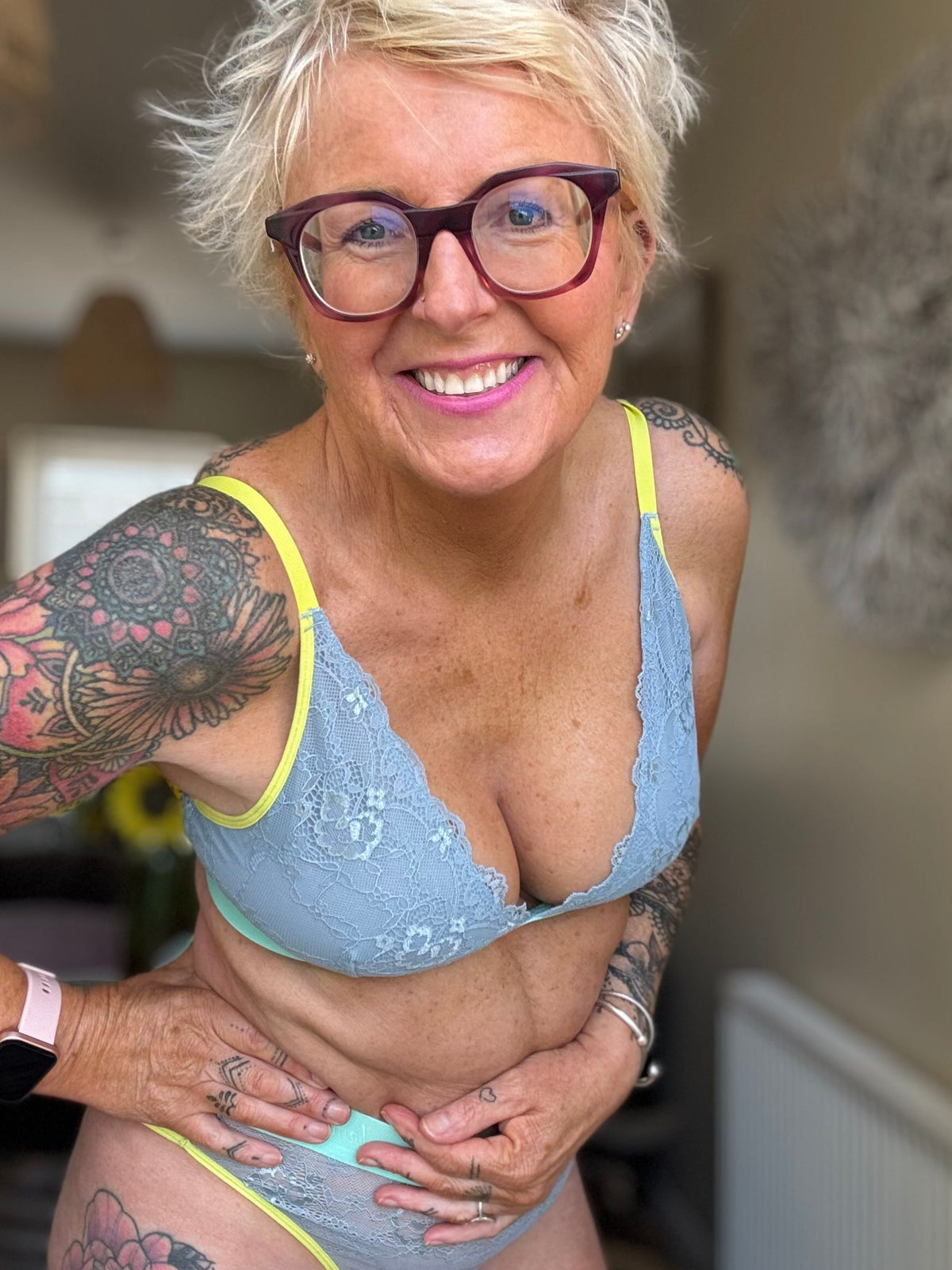 Woman wearing a light blue bra and underwear set with tattoos on arms and chest.