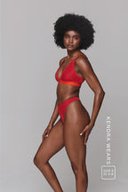 A woman standing with her side to wearing a red lace bralette paired with matching knickers
