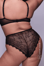A woman standing with her back turned is modelling a Black Lace Short paired with a Black lace bralette 