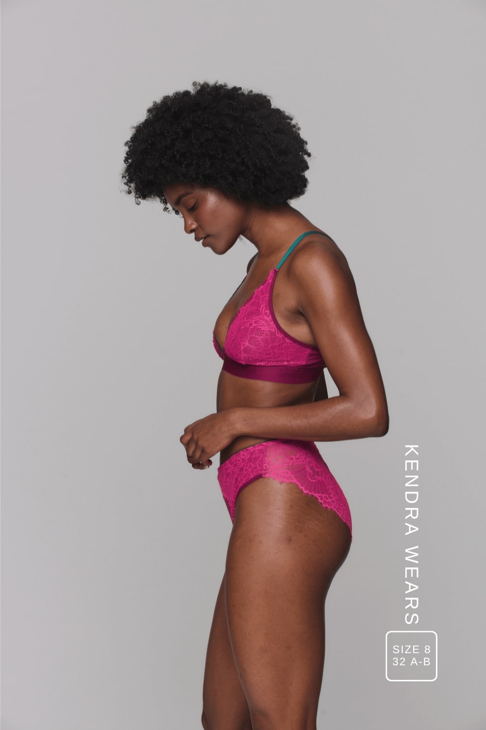 A woman standing with her side to wearing a pink lace lingerie set 