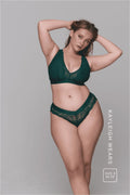 A woman standing front to with her arms up in her hair modelling a dark green lace lingerie set