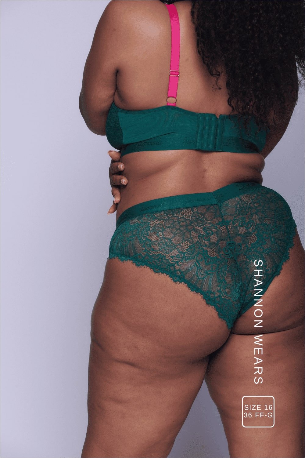 A close up of the back of a woman wearing a dark green lingerie set with pink straps 